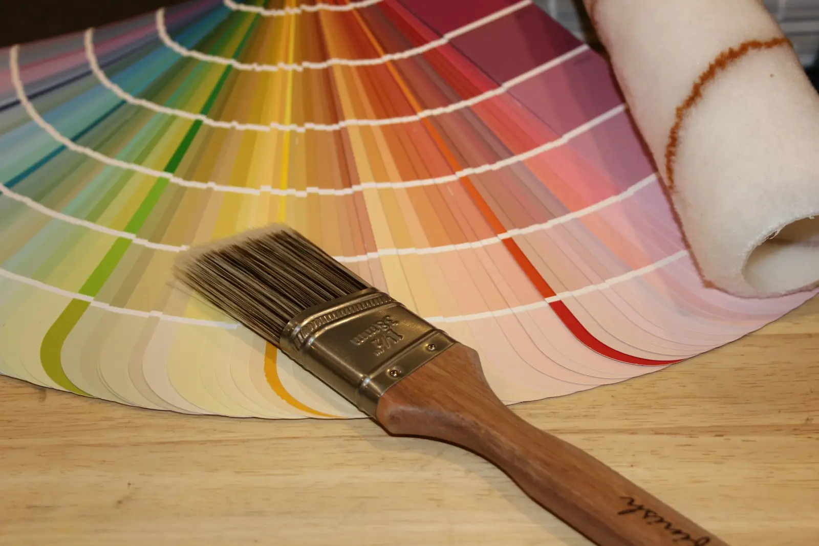 Paintbrush and roller beside a fan of paint colour swatches
