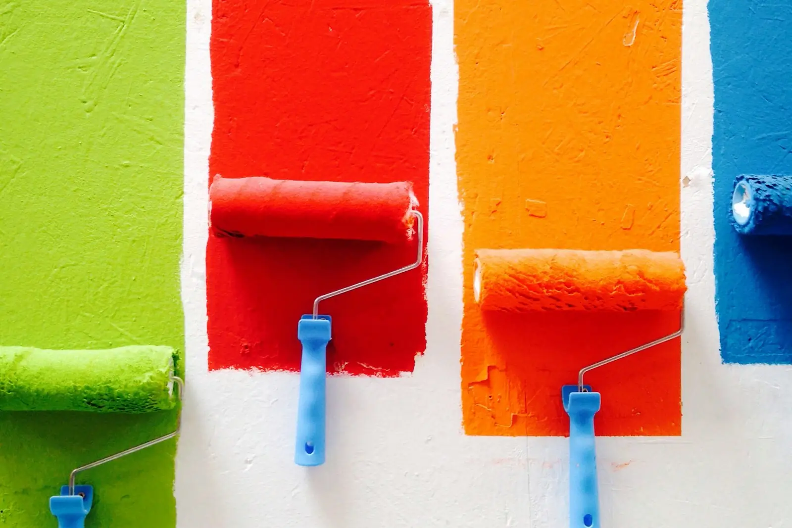 Four rollers painting bright stripes of colour on a wall