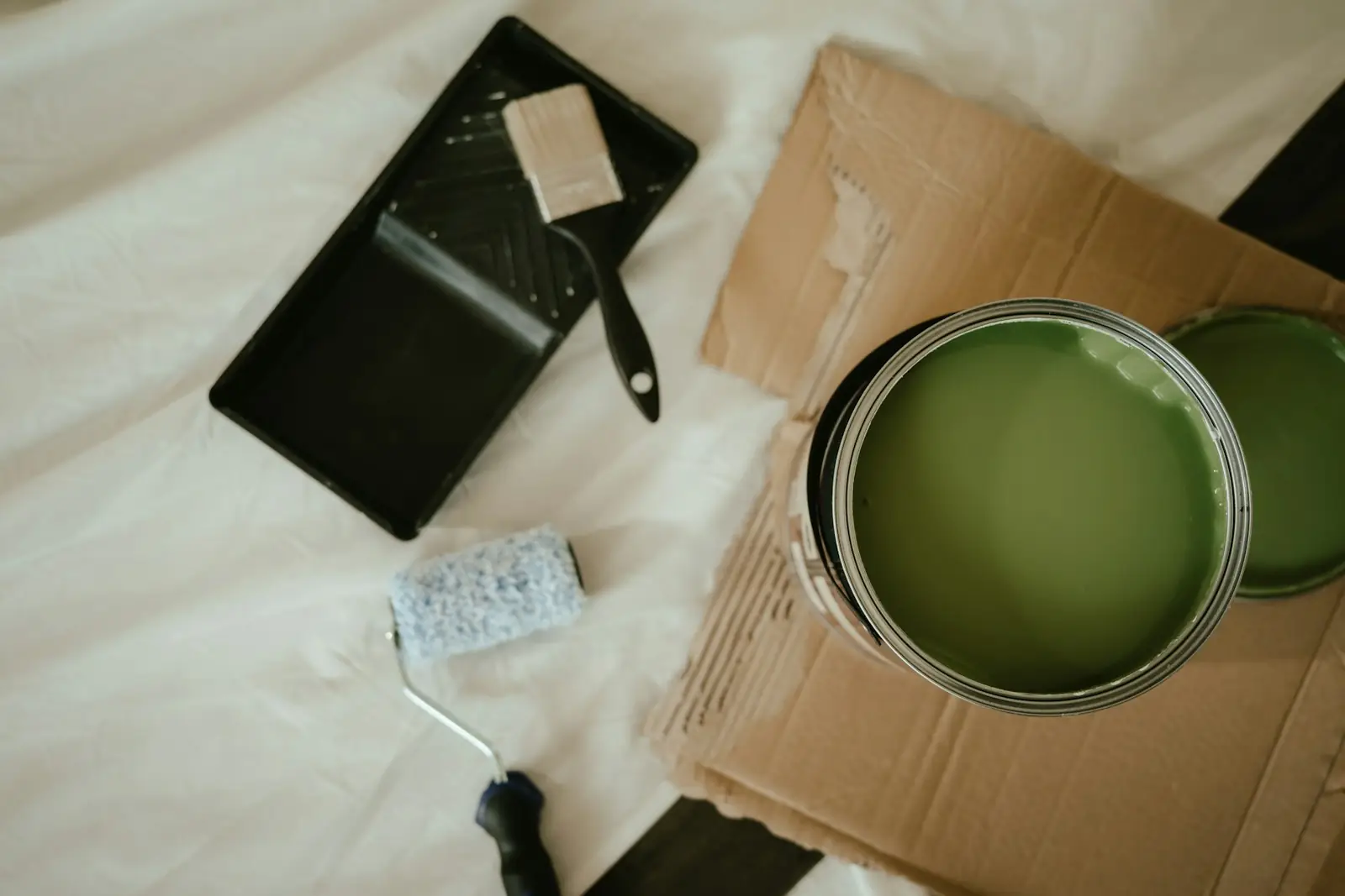 Open tin of green paint with a roller tray and brush on a dust sheet