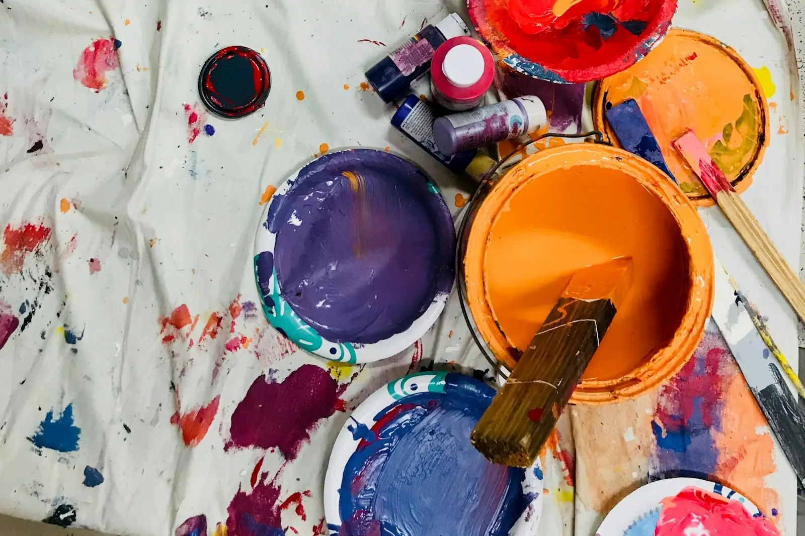 Open paint tins and brushes on a paint-spattered dust sheet