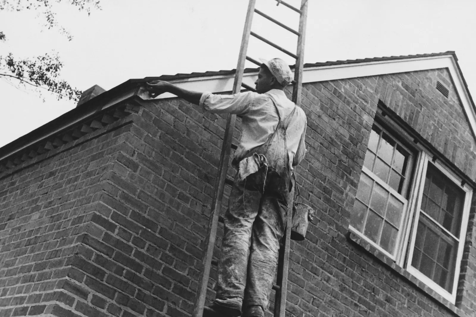 Painter on a ladder painting the fascia boards of a brick house