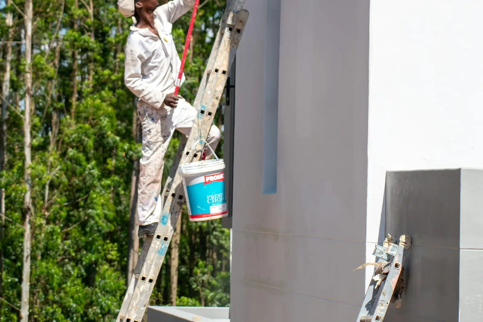 Painter using a roller on an extension pole to reach a high exterior wall