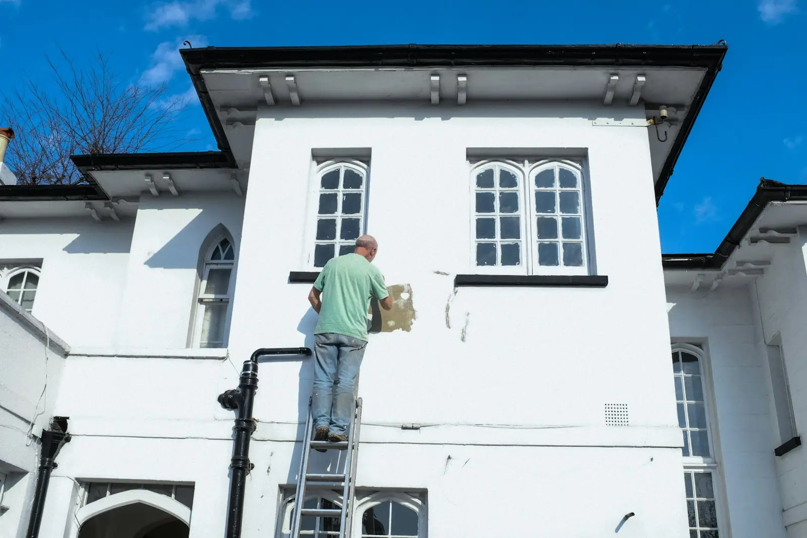 Painter on a ladder repainting the white rendered exterior of a house
