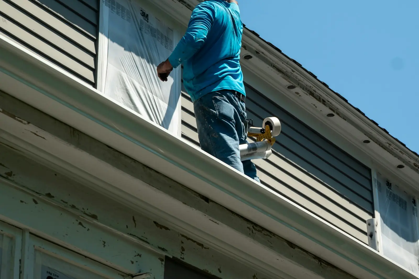 Painter masking a window with protective sheeting before exterior painting