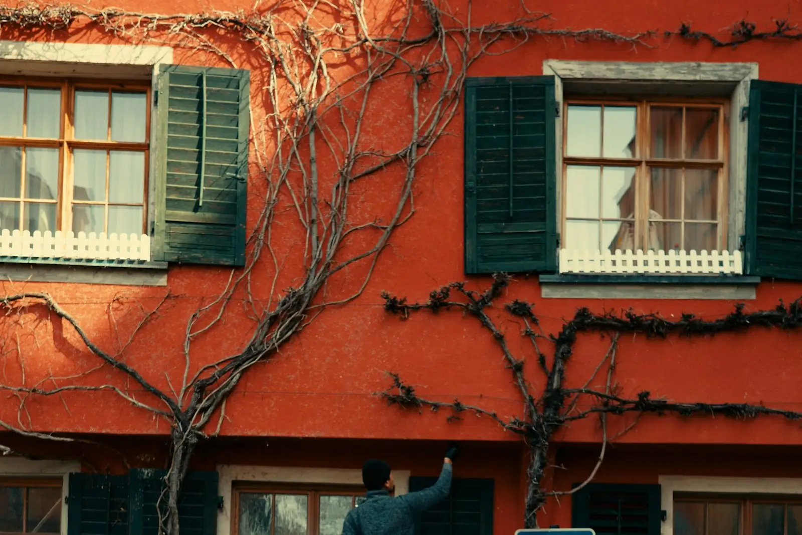 Painter on a stepladder painting a red facade with dark green shutters