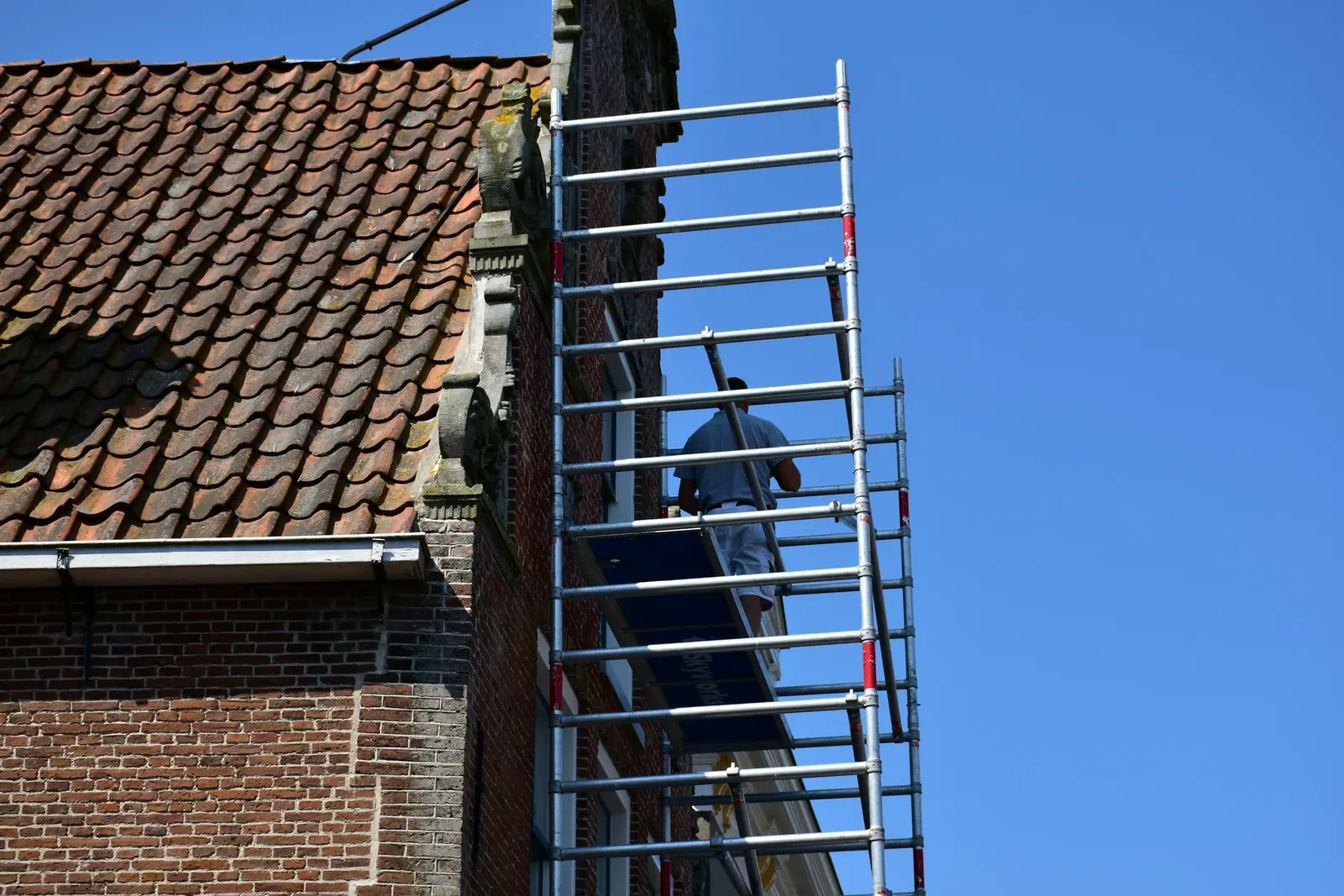 Painter working from an aluminium scaffold tower beside the gable of a brick house