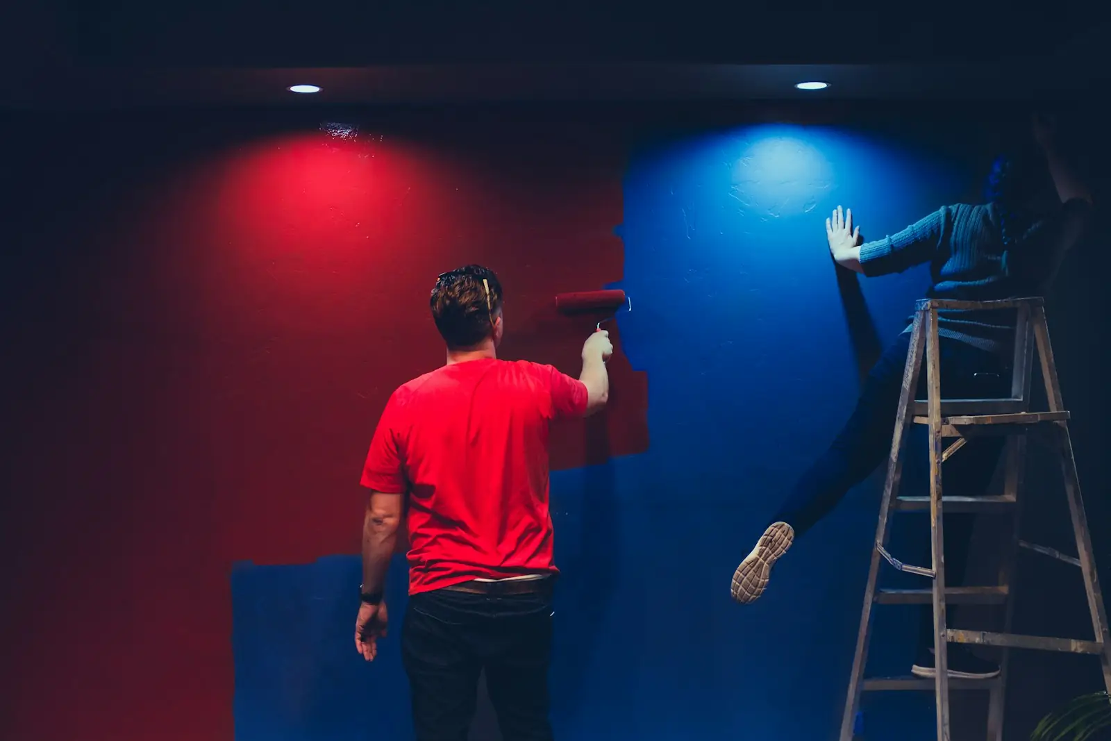Two decorators painting a room in deep red and blue