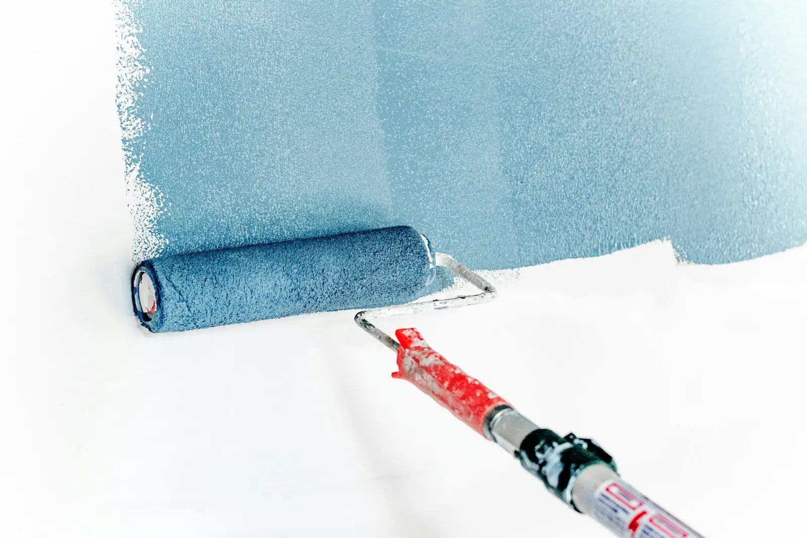 Paint roller applying a coat of blue paint to a white wall