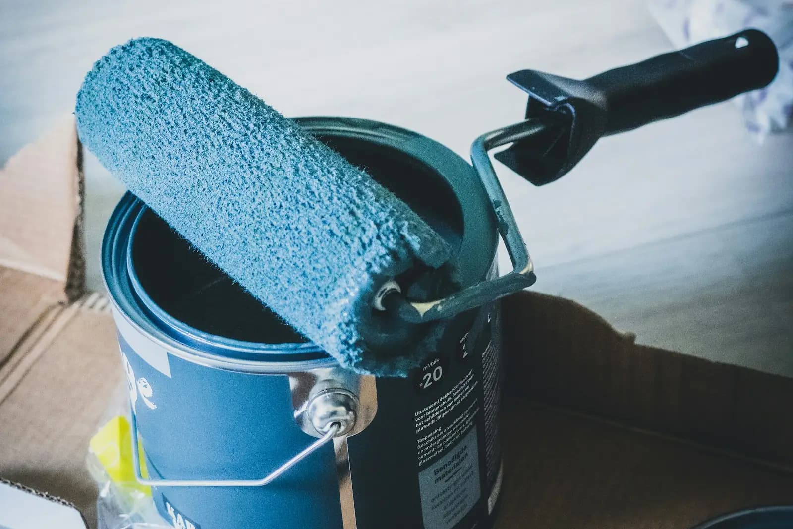 Paint roller resting on an open tin of blue paint
