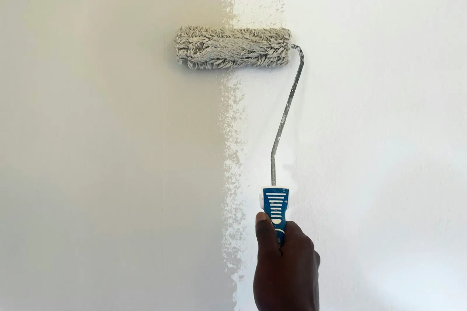 Roller applying a fresh coat of white emulsion to a wall